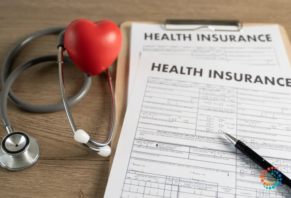 Helath insurance forms on a clipboard next to stethoscope